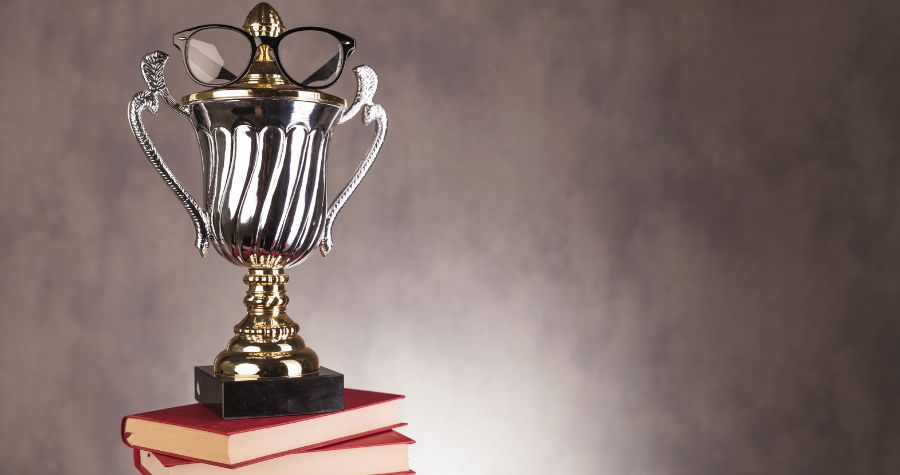 A golden trophy with glasses on it atop a stack of books