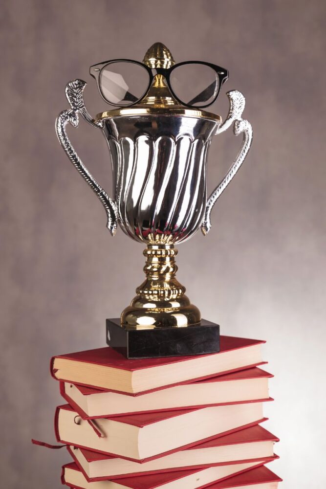 A golden trophy with glasses on it atop a stack of books