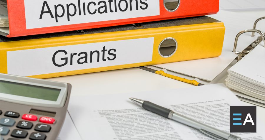 Two binders reading "applications" and "grants" stacked behind a calculator, pens, and paper