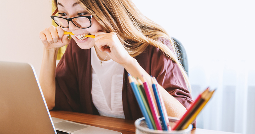 person biting a pencil in front of a laptop