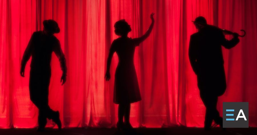 Three dark silhouettes of people in front of a red curtain