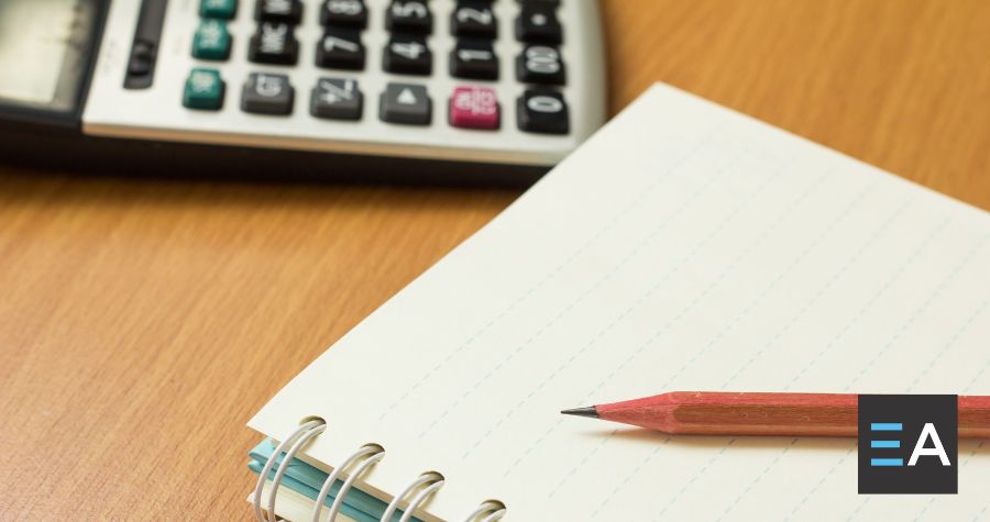 A notepad with a pencil resting on it next to a calculator 