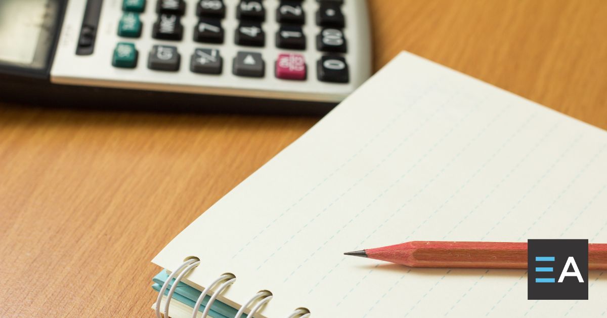 A notepad with a pencil resting on it next to a calculator