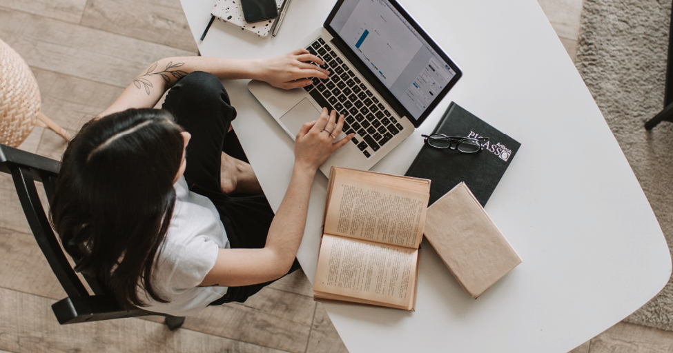 person at desk with computer and books