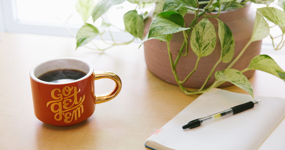 mug next to a plant and pen and paper