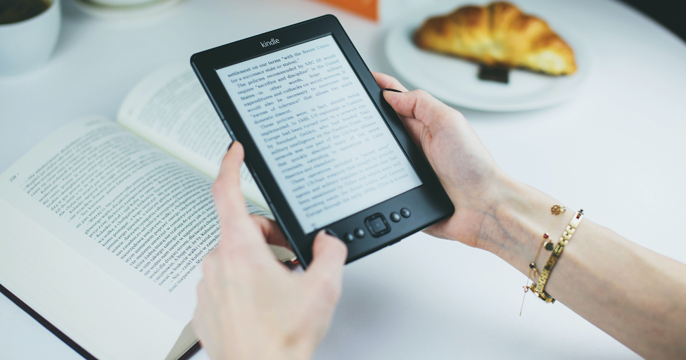 person holding a kindle over a physical book