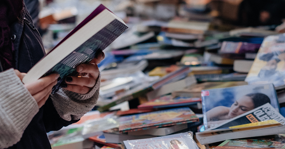 a person looking at a book with a big table of books nearby