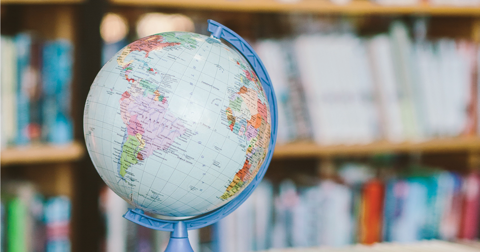 a globe stacked on some books with a bookshelf in the background