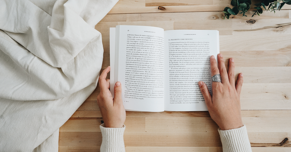 hands holding an open book on a table.